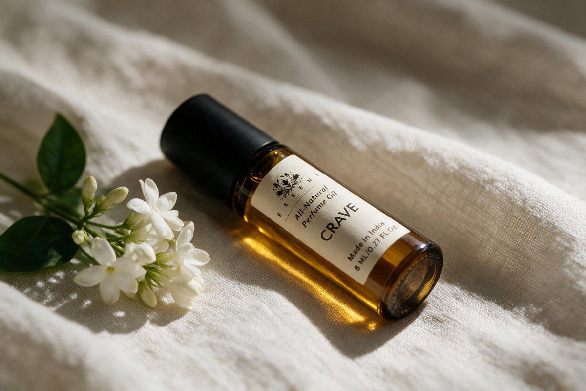 Essent Crave roll-on attar lying on ivory linen beside white jasmine